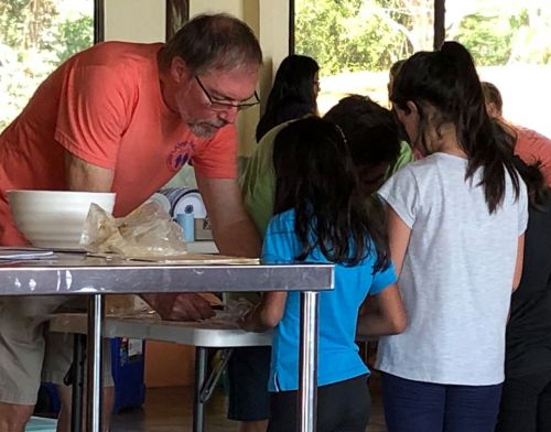 A man assists children with an activity at a table in a bright, indoor space.