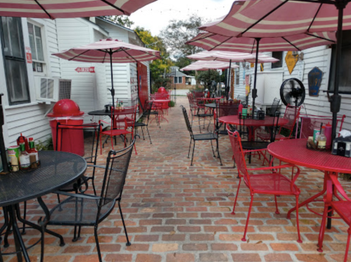 Outdoor dining area with red and black tables, chairs, and umbrellas on a brick pathway.