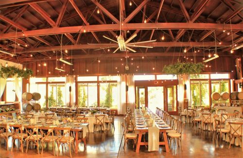 A spacious event venue with wooden beams, long dining tables, and large windows letting in natural light.