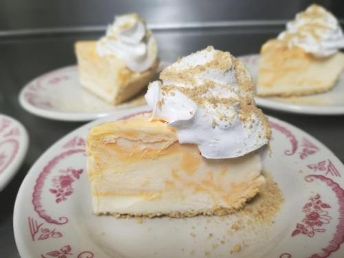 A slice of creamy orange cheesecake topped with whipped cream and graham cracker crumbs on a decorative plate.