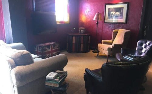 Cozy living room with a mix of seating, a lamp, and colorful decor against a deep red wall.