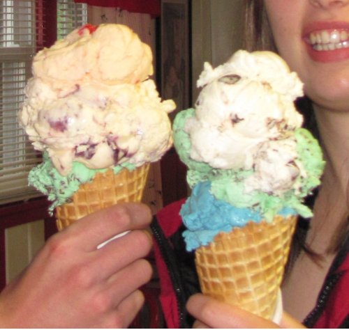 Two ice cream cones held by a person, featuring colorful scoops of pink, white, and mint green ice cream.