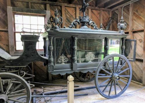 A vintage horse-drawn carriage displayed in a rustic barn, featuring ornate details and large wooden wheels.