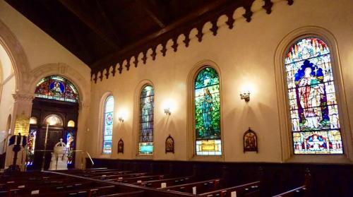 Interior of a church featuring stained glass windows, wooden pews, and decorative wall elements.