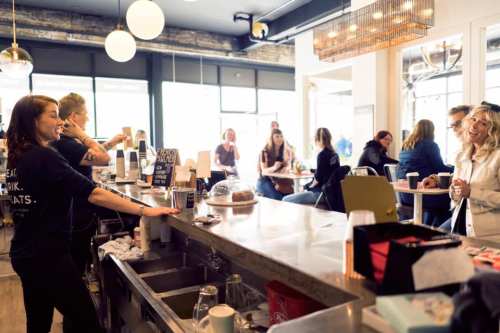 A busy café scene with a barista serving customers at the counter, while patrons chat and enjoy their drinks.