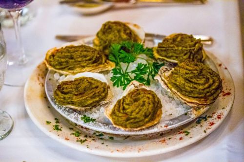 A plate of baked oysters topped with a green herb mixture, garnished with parsley, on a bed of ice.