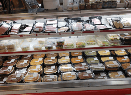 A display case filled with various packaged meats, salads, and prepared meals in clear containers.