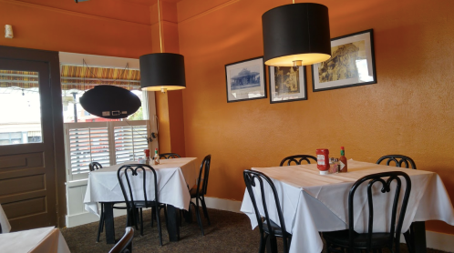 Cozy restaurant interior with orange walls, black lamps, and white tablecloths on round tables. Ketchup and hot sauce on tables.