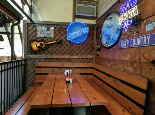 A cozy wooden dining area with a large table, neon signs, and rustic decor in a casual restaurant setting.
