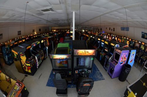 A wide view of a retro arcade filled with numerous classic arcade game machines and colorful screens.