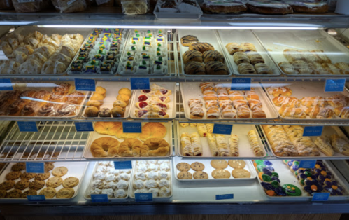 A display case filled with various baked goods, including cookies, pastries, and colorful desserts.