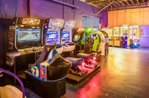 A row of colorful arcade games with bright screens and illuminated controls in a dimly lit game room.