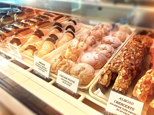 A display case filled with various pastries, including cream puffs, almond crescents, and swans, all beautifully arranged.