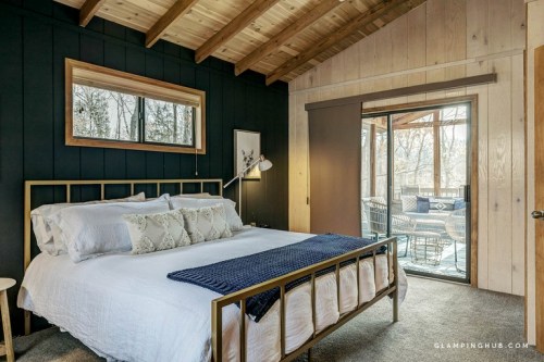 Cozy bedroom with a wooden ceiling, dark walls, a large bed, and sliding glass doors leading to an outdoor deck.