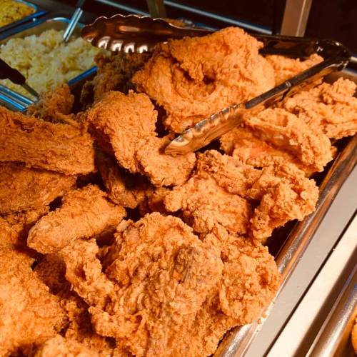 A close-up of a tray filled with crispy, golden-brown fried chicken pieces, with tongs resting on top.