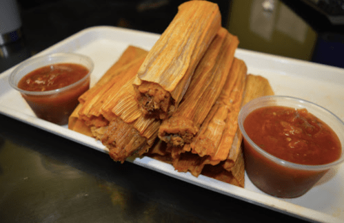A plate of stacked tamales with two cups of red salsa on the side.