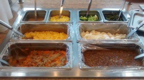 A buffet-style food station with various trays of macaroni and cheese, vegetables, and meat dishes.