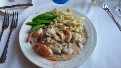 A plate of shrimp in creamy sauce with fettuccine and green snap peas, served on a white tablecloth.
