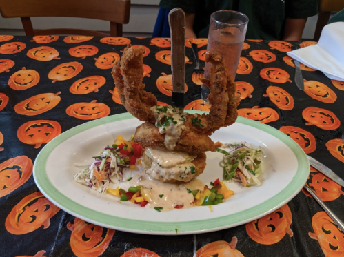 A plate of fried seafood with a knife, served on a Halloween-themed tablecloth with pumpkins.