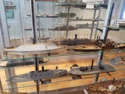 Display case filled with detailed ship models, showcasing various historical vessels in a museum setting.