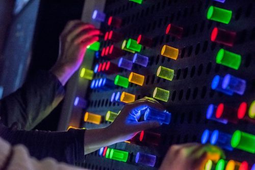Hands interacting with a colorful, illuminated panel featuring various glowing buttons in vibrant hues.