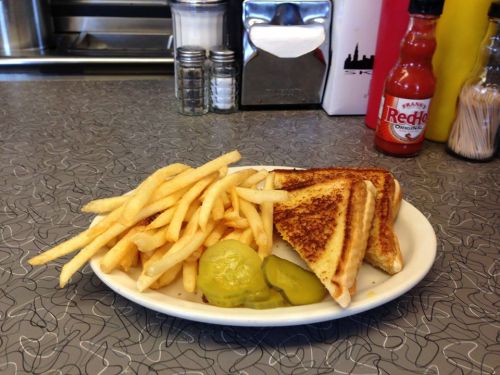 A plate with grilled cheese sandwiches, French fries, and pickles, set on a retro diner table.