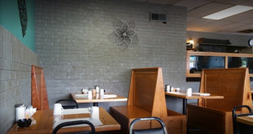 Cozy restaurant interior with wooden booths, tables set for dining, and a decorative flower on the wall.