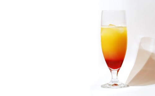 A tall glass filled with a gradient drink, transitioning from red at the bottom to yellow at the top, with ice cubes.