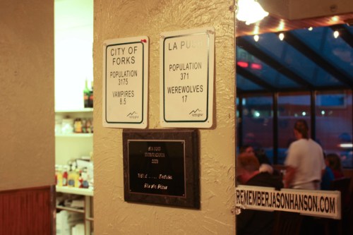 Signs on a wall display population stats for Forks (vampires) and La Push (werewolves) in a cozy restaurant setting.
