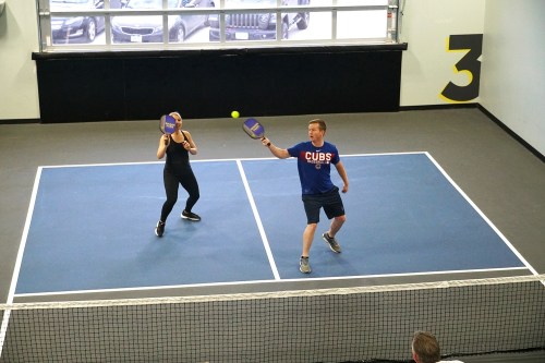 Two people playing pickleball on an indoor court, with paddles raised and a ball in play.