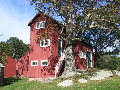 A red two-story building with white windows, surrounded by trees and grass under a clear blue sky.