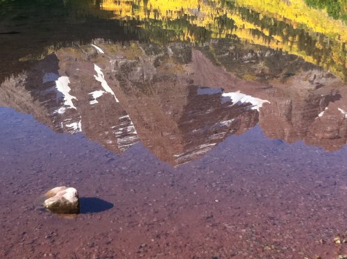 A serene mountain reflection in calm water, with vibrant autumn colors and a small rock in the foreground.