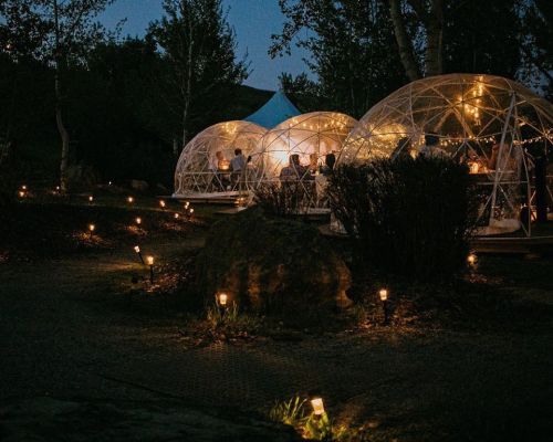 Cozy outdoor dining igloos illuminated at night, surrounded by soft glowing lights and greenery.