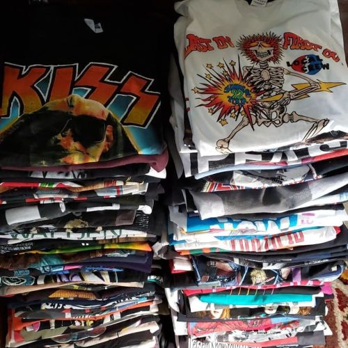 A large stack of folded graphic t-shirts featuring various band designs and colorful prints.