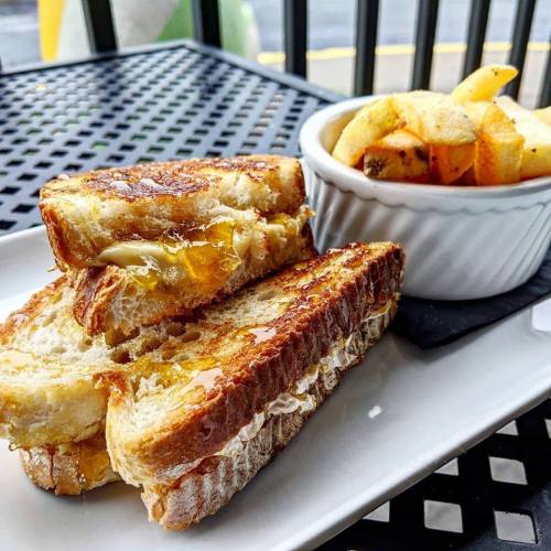 A plate with two golden grilled cheese sandwiches and a side of crispy fries in a white bowl.
