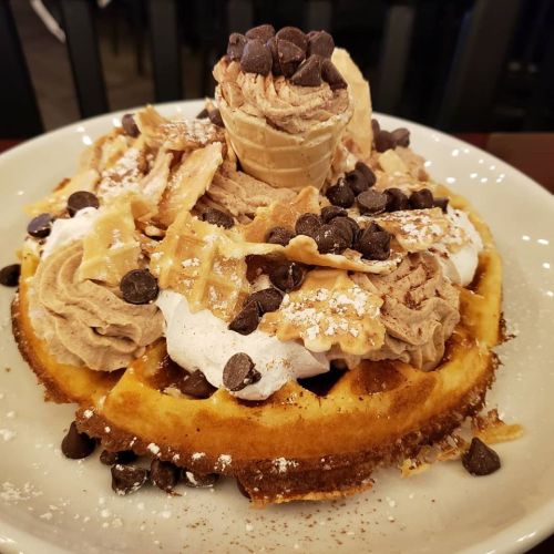 A decadent waffle topped with whipped cream, chocolate mousse, mini waffle pieces, and chocolate chips.