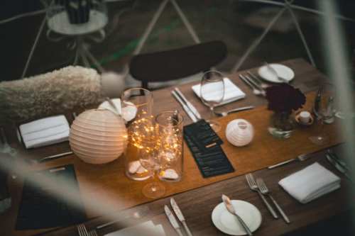 A beautifully set dining table with candles, lanterns, and elegant tableware, creating a cozy atmosphere.