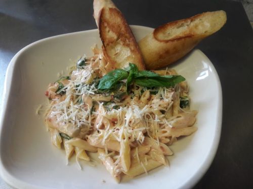 A bowl of creamy pasta with basil, topped with grated cheese, accompanied by two slices of toasted bread.