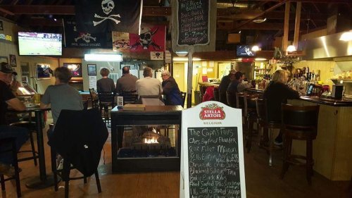 A cozy bar scene with patrons seated at the counter, pirate-themed decor, and a chalkboard menu in the foreground.