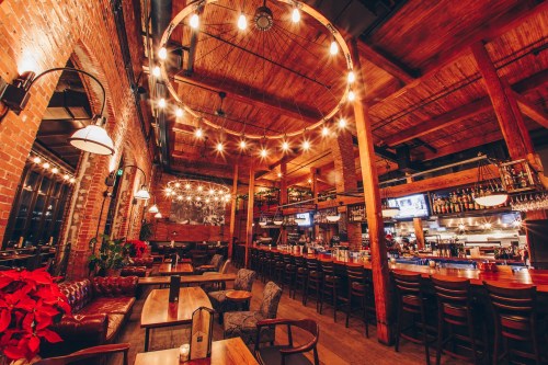 Cozy restaurant interior with wooden beams, warm lighting, and a bar area, featuring brick walls and comfortable seating.