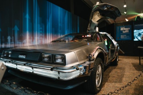 A DeLorean car with its gullwing doors open, displayed in a futuristic setting with digital graphics in the background.