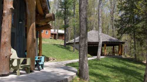 A serene outdoor scene featuring rustic cabins and a gazebo surrounded by trees and green grass.