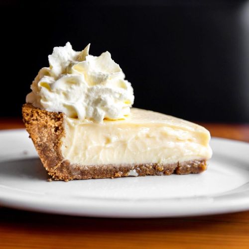 A slice of creamy cheesecake topped with whipped cream on a white plate.