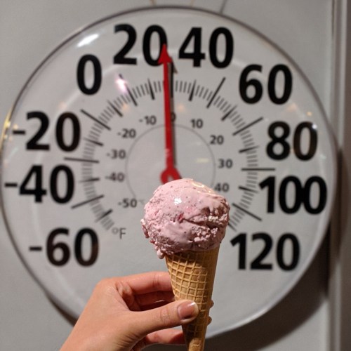 A hand holds a pink ice cream cone in front of a thermometer reading 20°F.