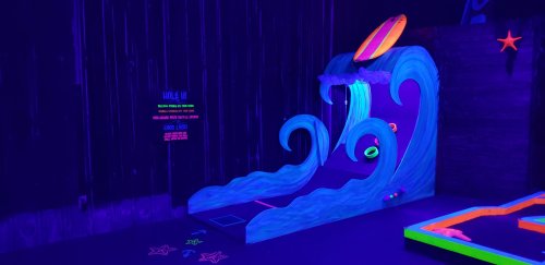 A brightly colored mini-golf hole featuring a wave design, glowing under black light, with colorful rings and decorations.