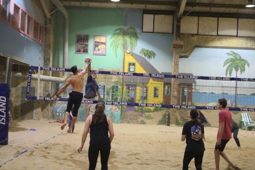 A group of people playing beach volleyball indoors, with colorful murals and a sandy court in the background.
