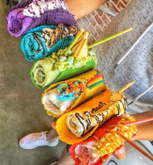 A colorful assortment of rolled ice cream in various flavors, served in vibrant waffle cones.