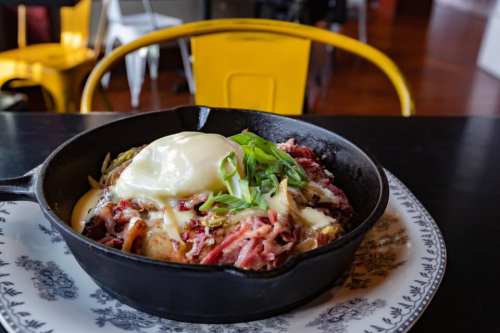 A cast iron skillet filled with savory meat, cheese, and a poached egg, garnished with green onions on a decorative plate.
