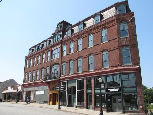 Historic brick building with multiple stories, large windows, and a decorative roofline, set against a clear blue sky.
