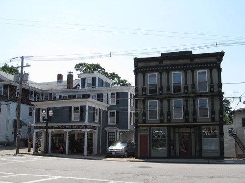 Two historic buildings at a street corner, one with a dark facade and the other in light blue, under a clear sky.